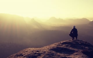 Hiker sits on a rocky peak and enjoy the mountains scenery - Annette Sloly Hypnotherapy